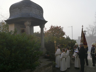 Die Wortgottesdienstleiterin und der Altardienst stehen vor dem Kriegerdenkmal.