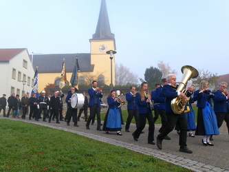 Festzug mit Musikbegleitung. Im Hintergrund sieht man die Kirche.